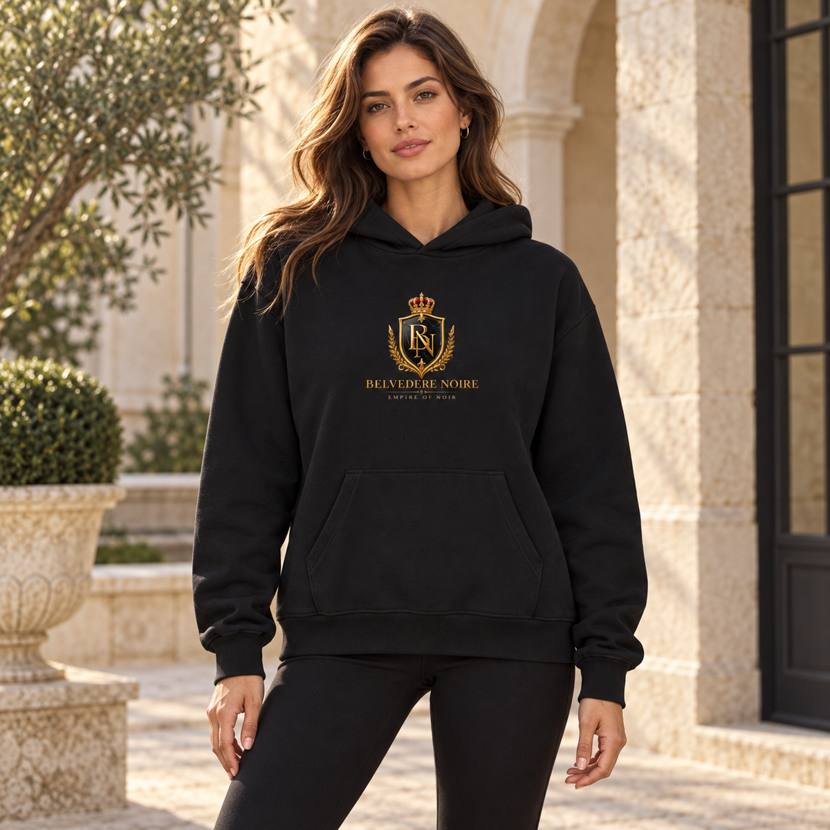 BELVEDERE NOIRE black centre crest hoodie, female model in courtyard, AI styling mockup